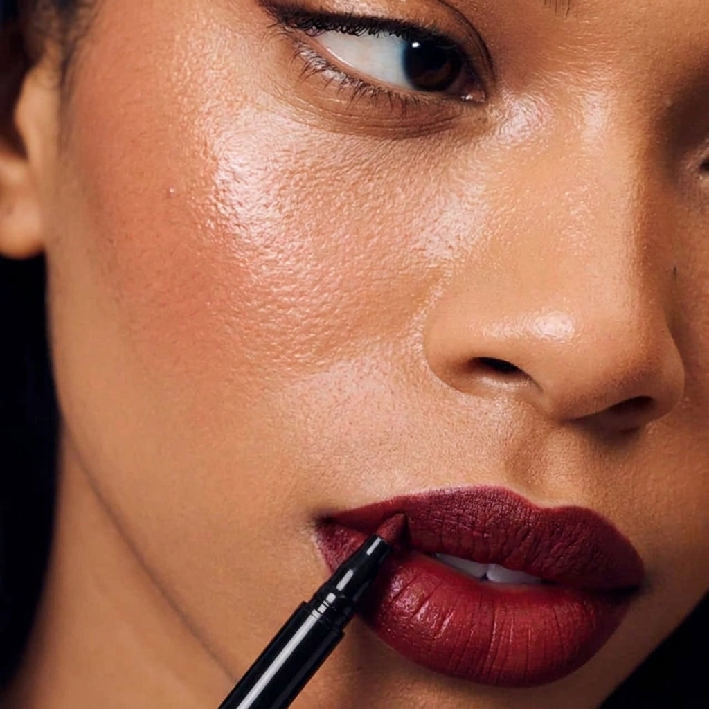 Gros plan : la pointe du crayon Lip Sculpt trace le contour d'une bouche rouge profond